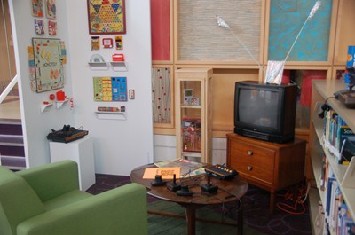 photo of chair, television with vintage Atari video game system with other games on wall. 