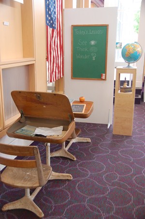 photo of vintage school room set up with wood desks, chalkboard, globe and bell. 