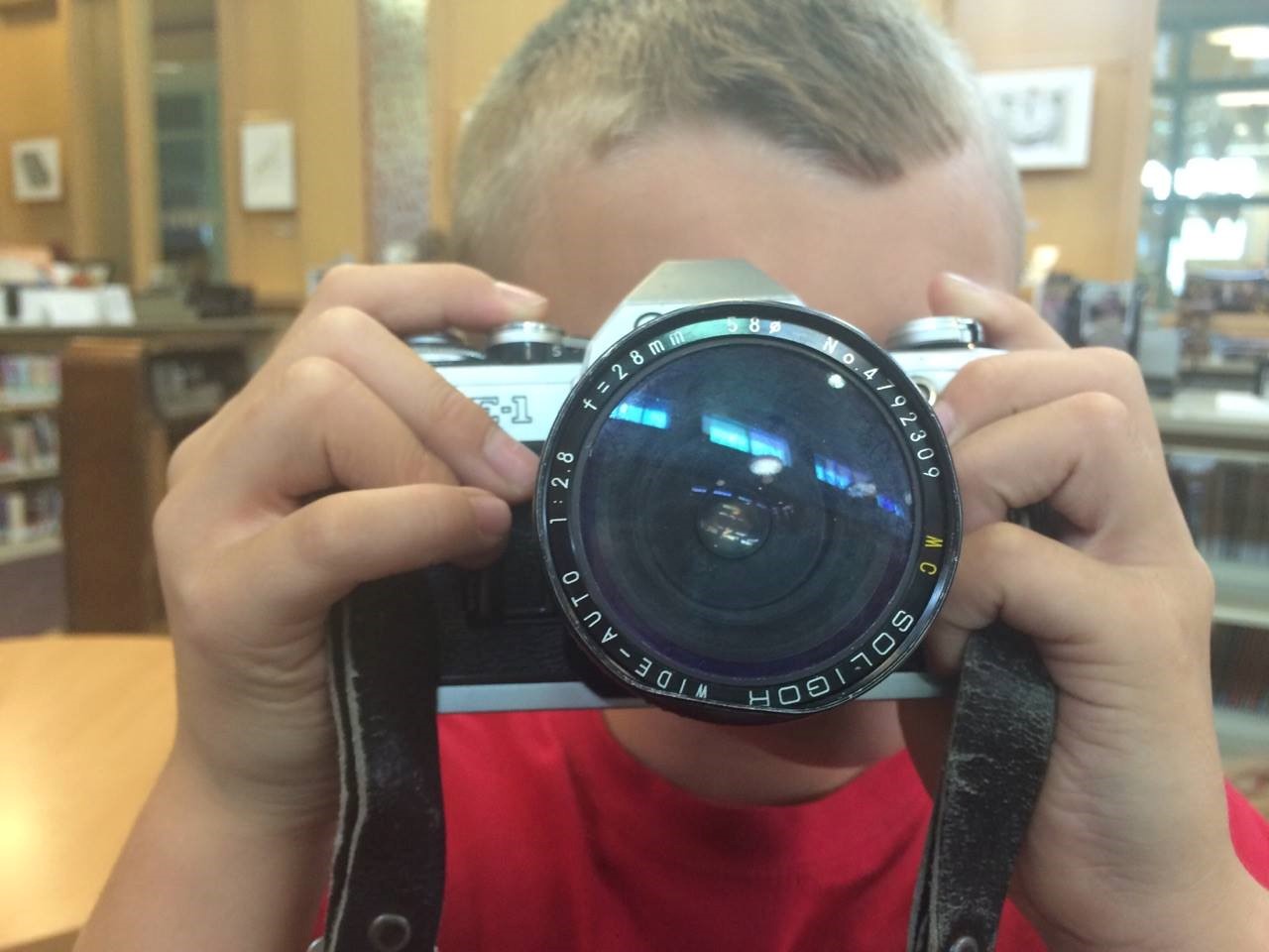 photo of student look directly at us through the lens of a large photo camera.