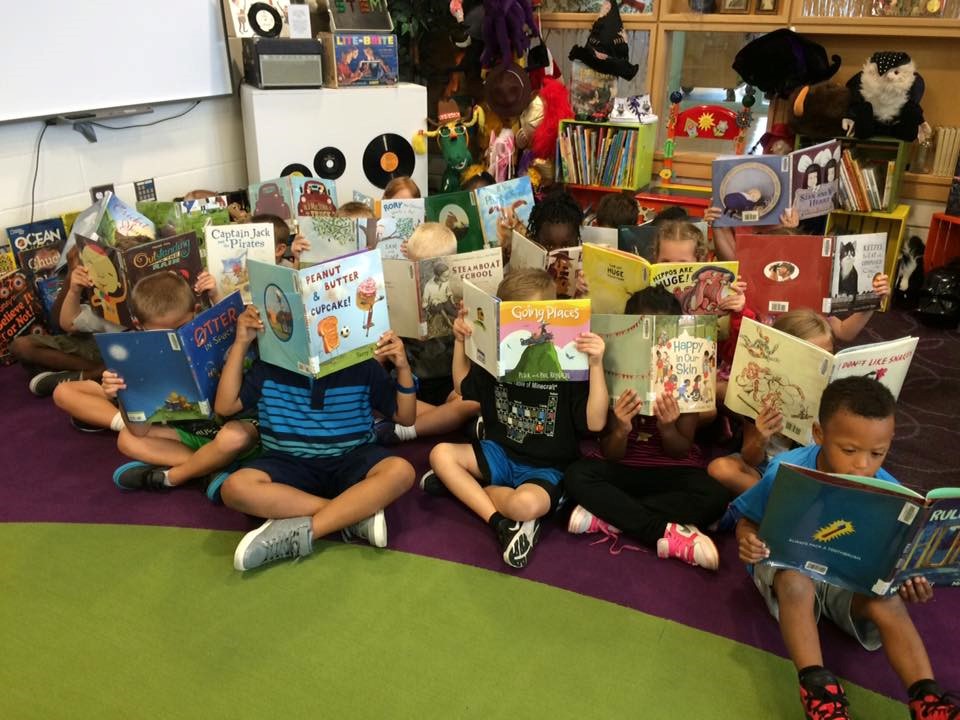 photo of large group of student reading books who are hiding their faces.