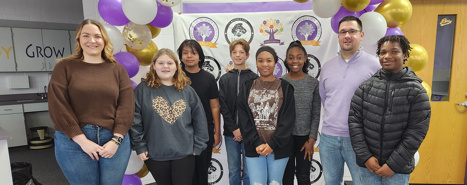 Students, assistant principal and principal pose in front of a banner and balloons after Raider of the Quarter recognition