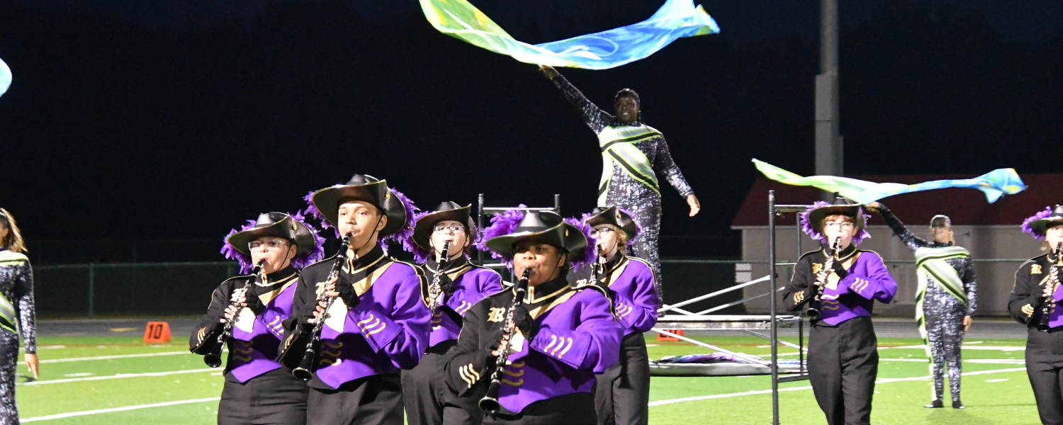 Band members and color guard march on the football field