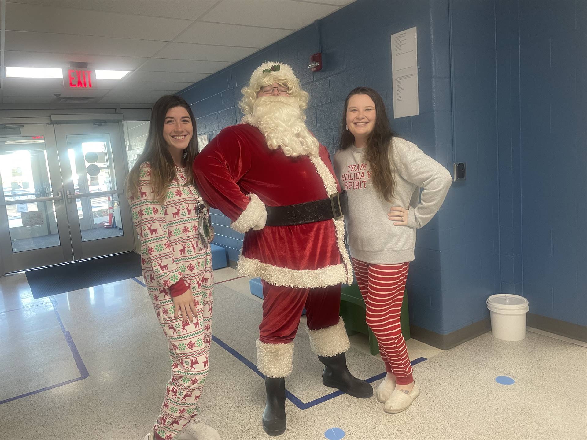 2 adult women in pajamas posing with Santa