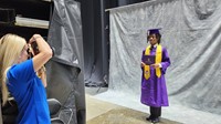 A graduate poses for photographer while holding diploma