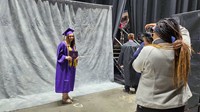 A graduate poses for photographer while holding diploma