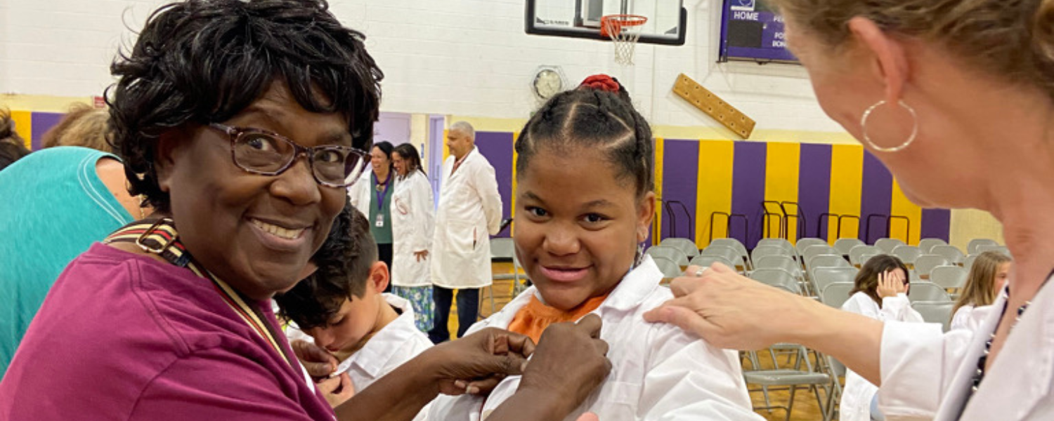 Family member smiles at the camera while pinning a student during a lab coat ceremony