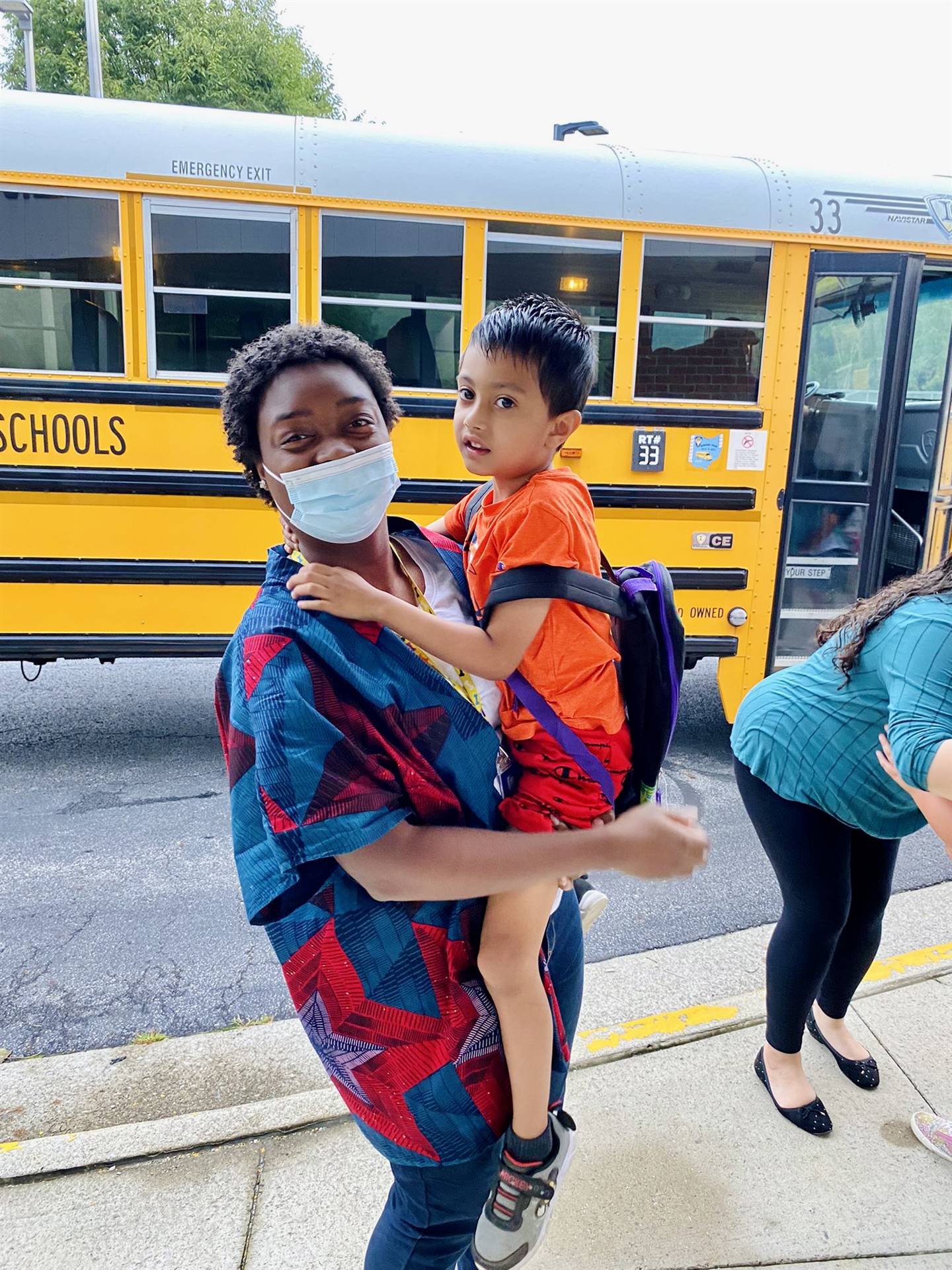 A woman holding a child in front of a school bus