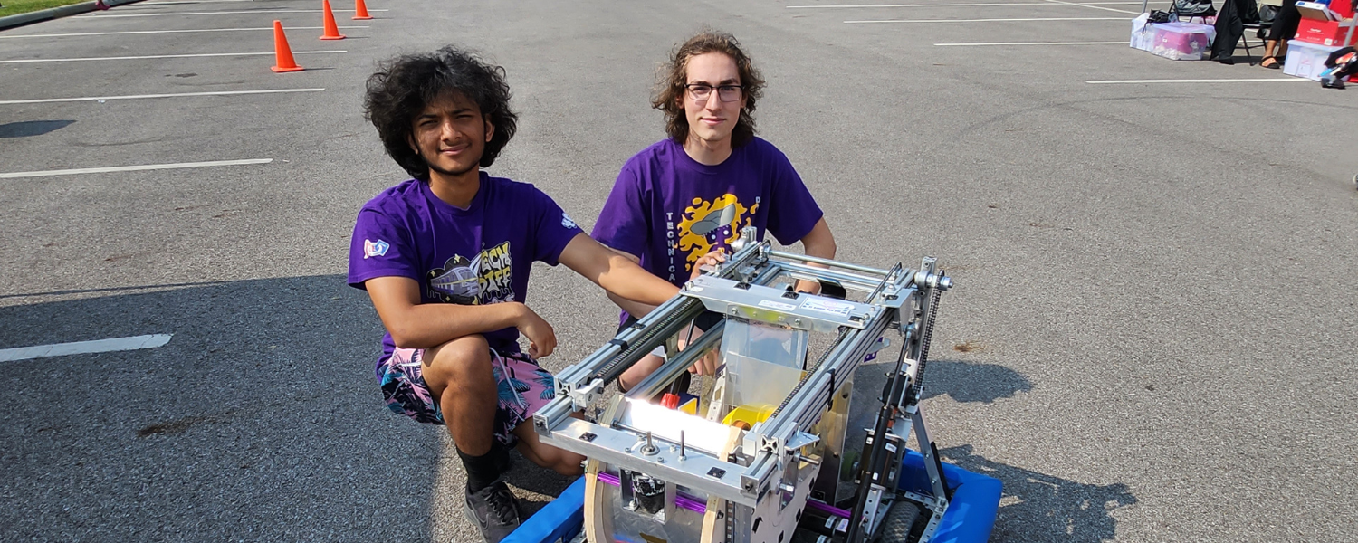 Two students on the high school robotics team pose with their robot