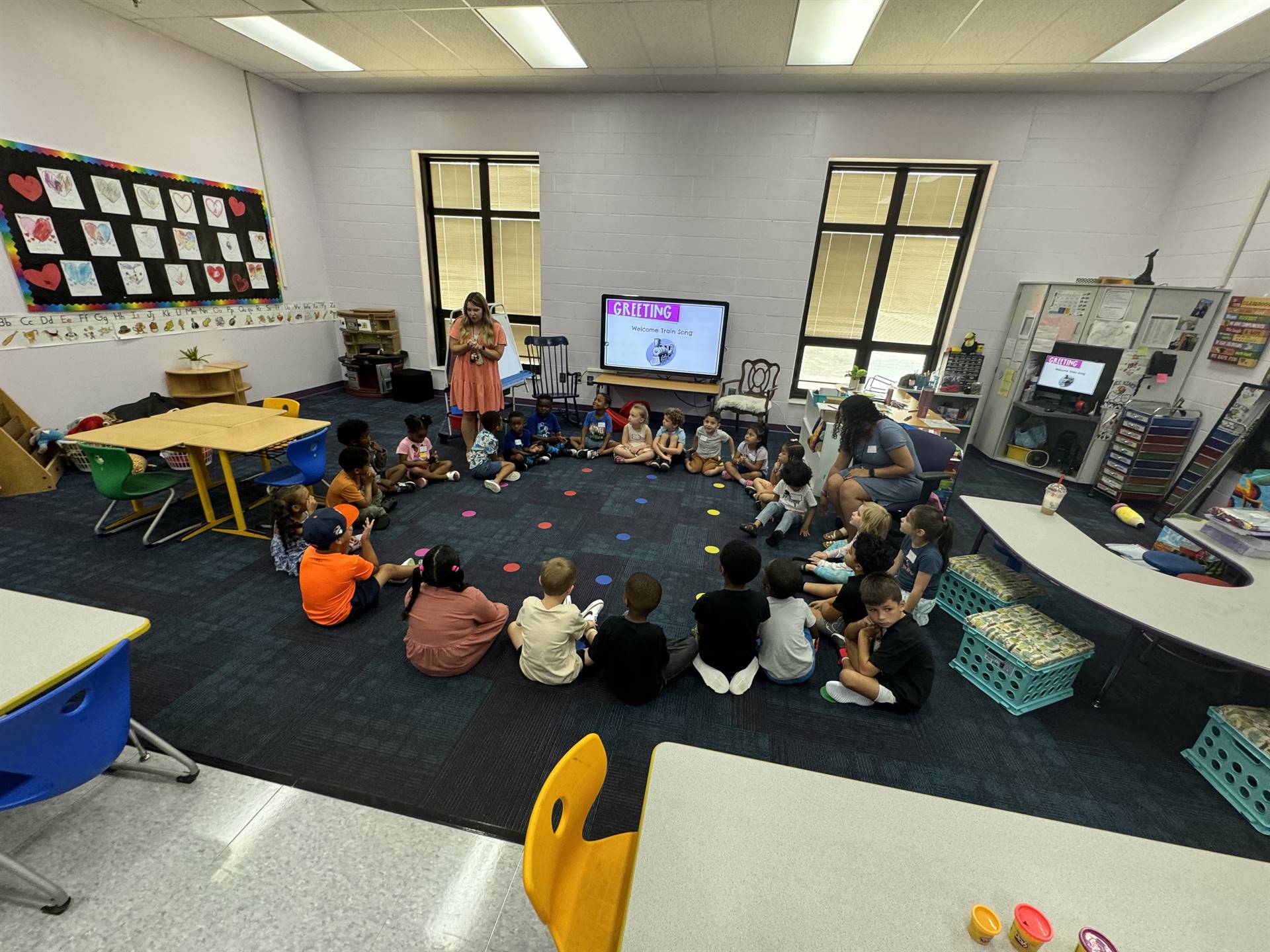 Kindergarteners listen to teachers in a circle.